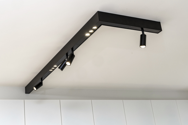 Detail van zwarte railverlichting in moderne witte keuken met vaste en richtbare spotjes.