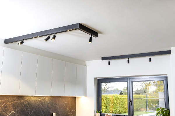 Detail van zwarte railverlichting met richtbare en vaste spotjes. Ingewerkte led-strip onder hangkasten als werkverlichting.
