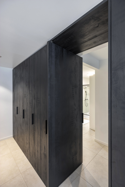 Kastenwand in zwarte houtkleur, zwarte grepen en pivotdeur naar berging.