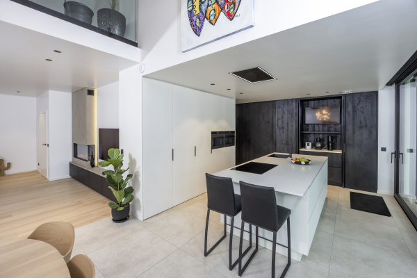 Lichte open keuken met maatwerk kasten, composiet werkblad en geïntegreerde ovens en koffiehoek.