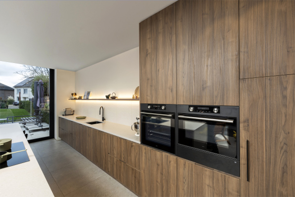 Kastenwand in donkere houtkleur met oven en microgolfoven. Tablet composiet wit. Zwevende legger met led-verlichting.