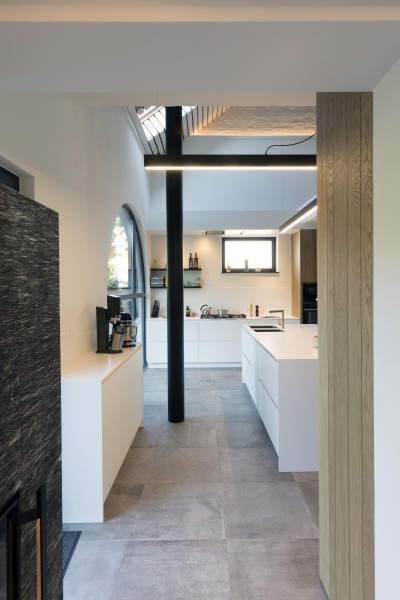 Strakke keuken in ruimte die open is tot in de nok draaitrap en gebogen raam witte gepoederlakte fronten en eik