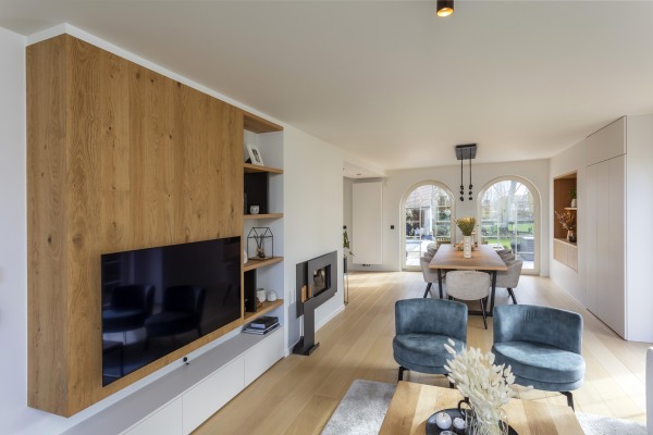 Woonkamer met maatwerk wandmeubel in eikenhout, geïntegreerde open vakken, tv-opstelling en moderne haard.